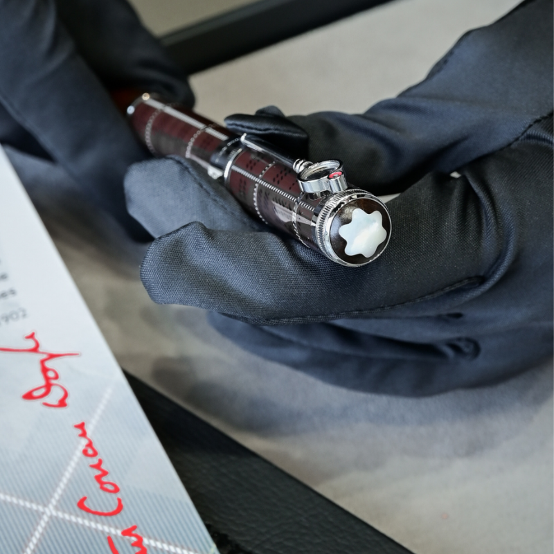 Manos con guantes negros sujetando una pluma Montblanc