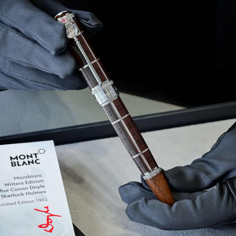 Pluma Montblanc de color marrón y plata, sostenida por manos con guantes